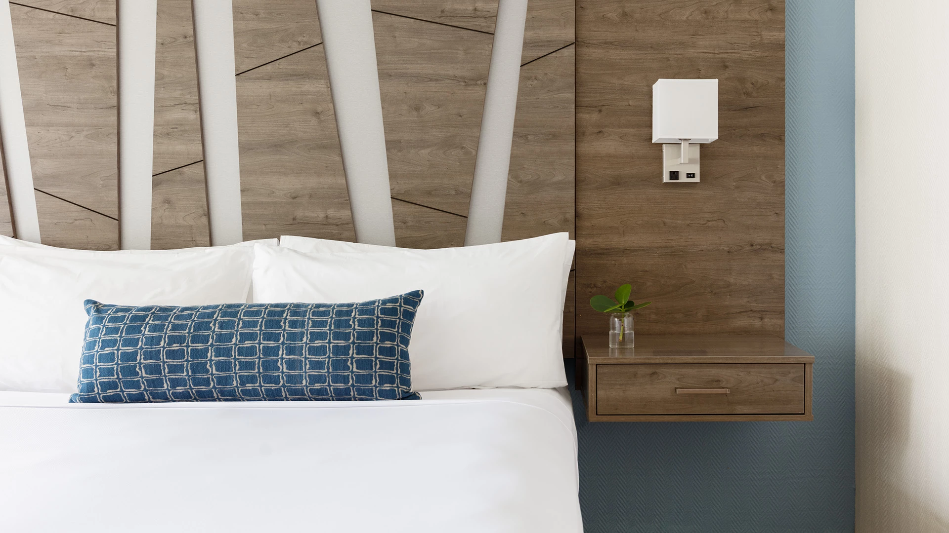a bed with white linens and a blue accent pillow