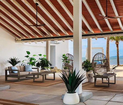A covered outdoor seating area with a wood ceiling, white walls, and a view of the water.