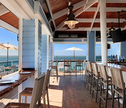 A bar with stools, a counter, and a selection of beverages, overlooking a body of water.