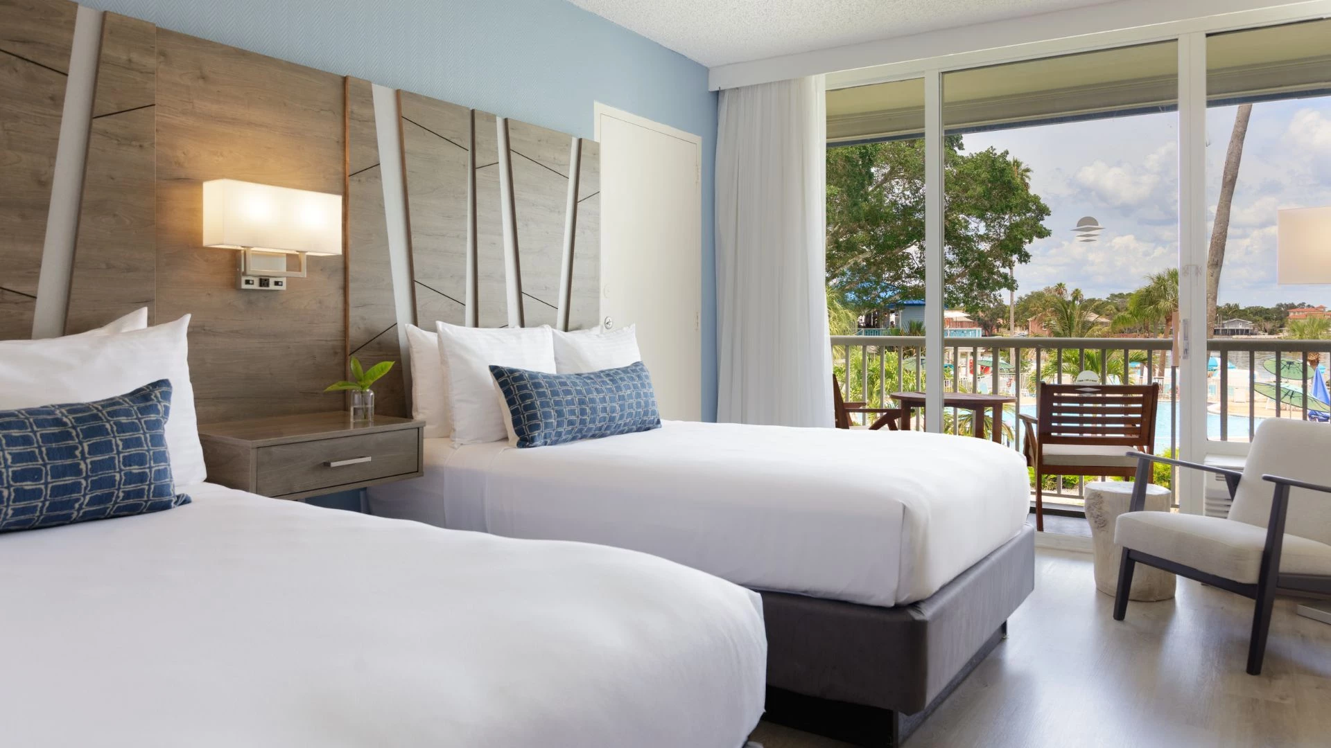 A hotel room with two beds, a balcony, and a view of the outdoors.