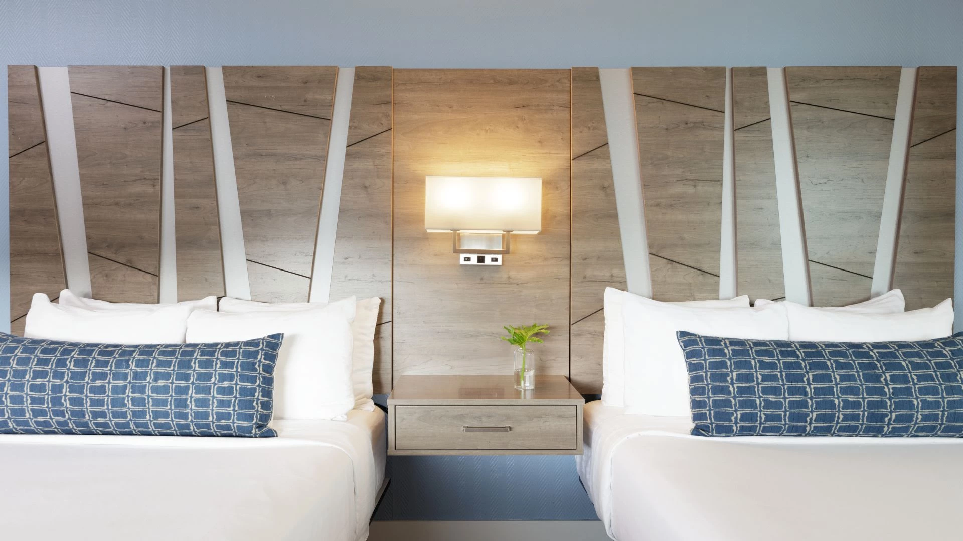 A close-up view of a hotel room with two beds, a nightstand, and a lamp.