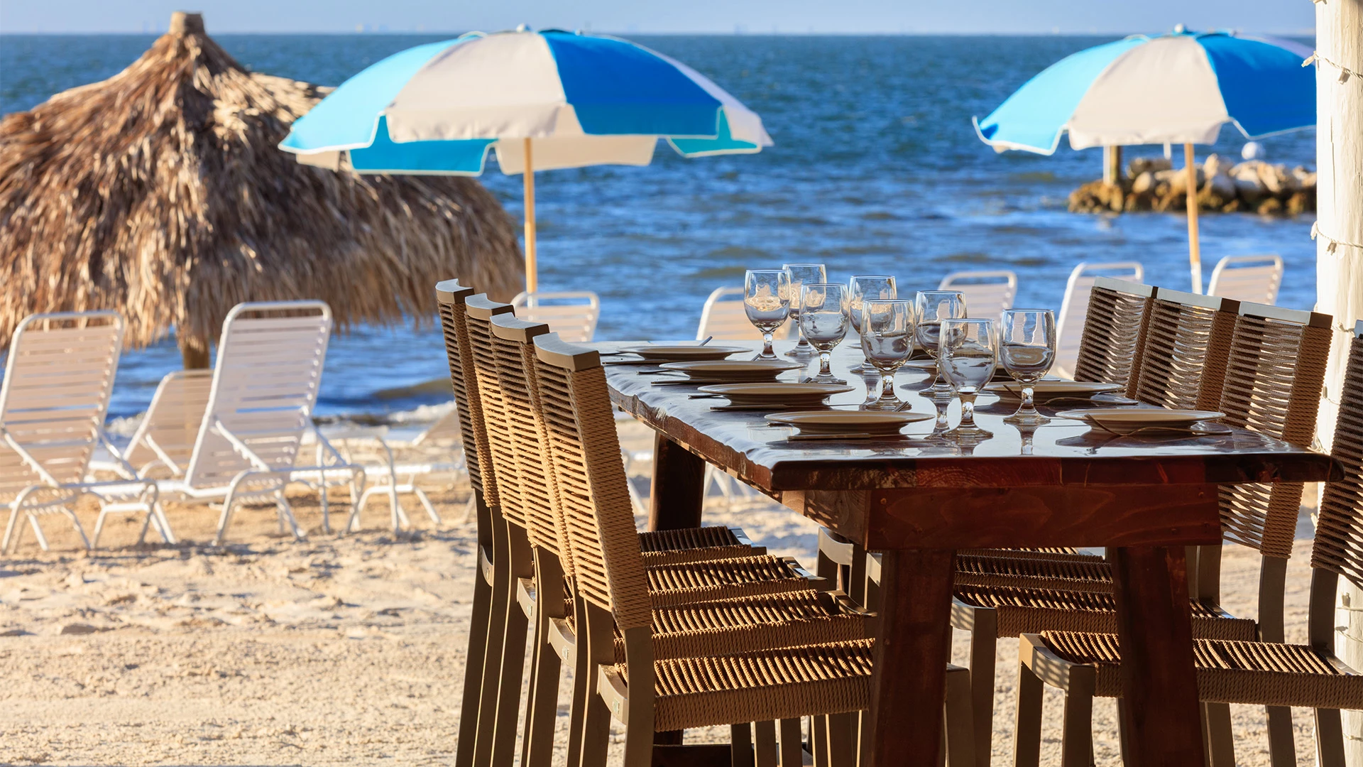 A beachside dining setup with a table, chairs, and umbrellas overlooking the ocean.