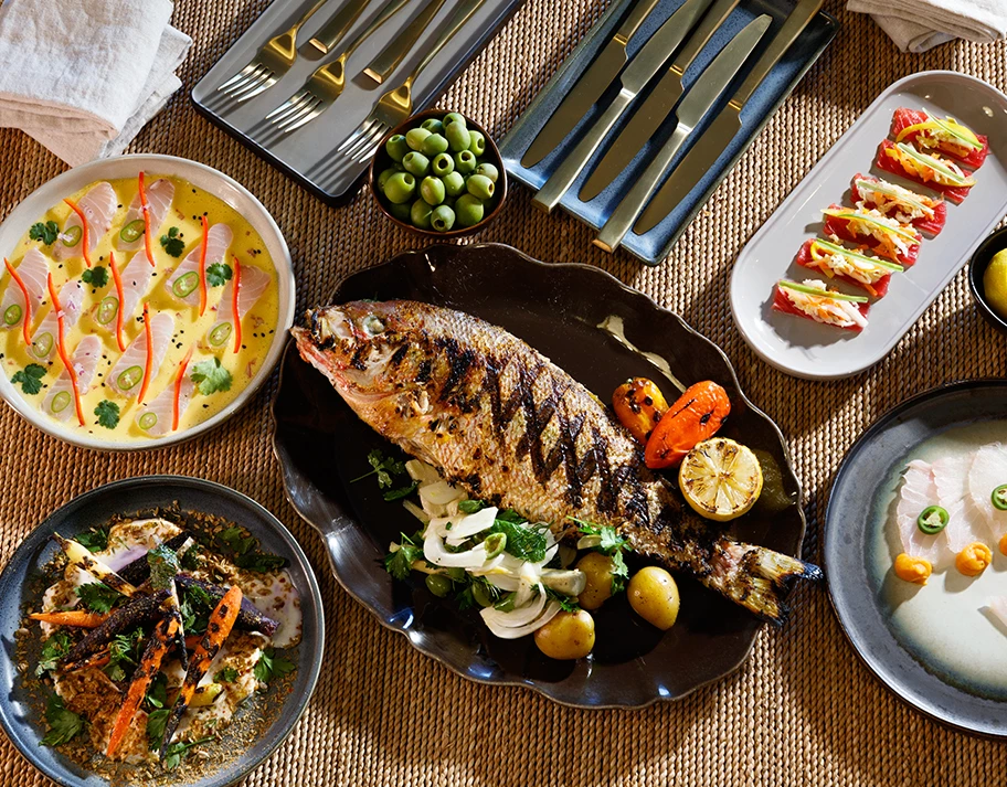 A beautifully set table with various dishes of food, including a grilled fish, vegetables, and other culinary delights.