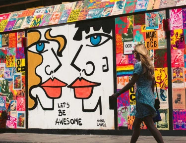 A colorful street art mural on the side of a building with a person walking by.