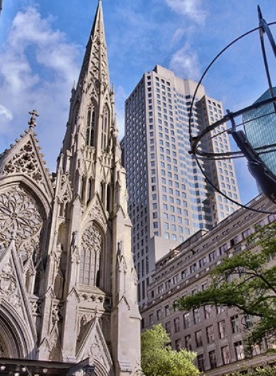 A cityscape with a church and skyscrapers under a blue sky with clouds.