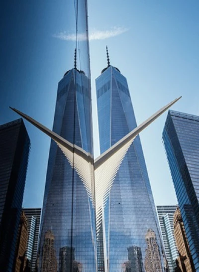 A cityscape photo showing several skyscrapers, including the One World Trade Center, under a clear blue sky.