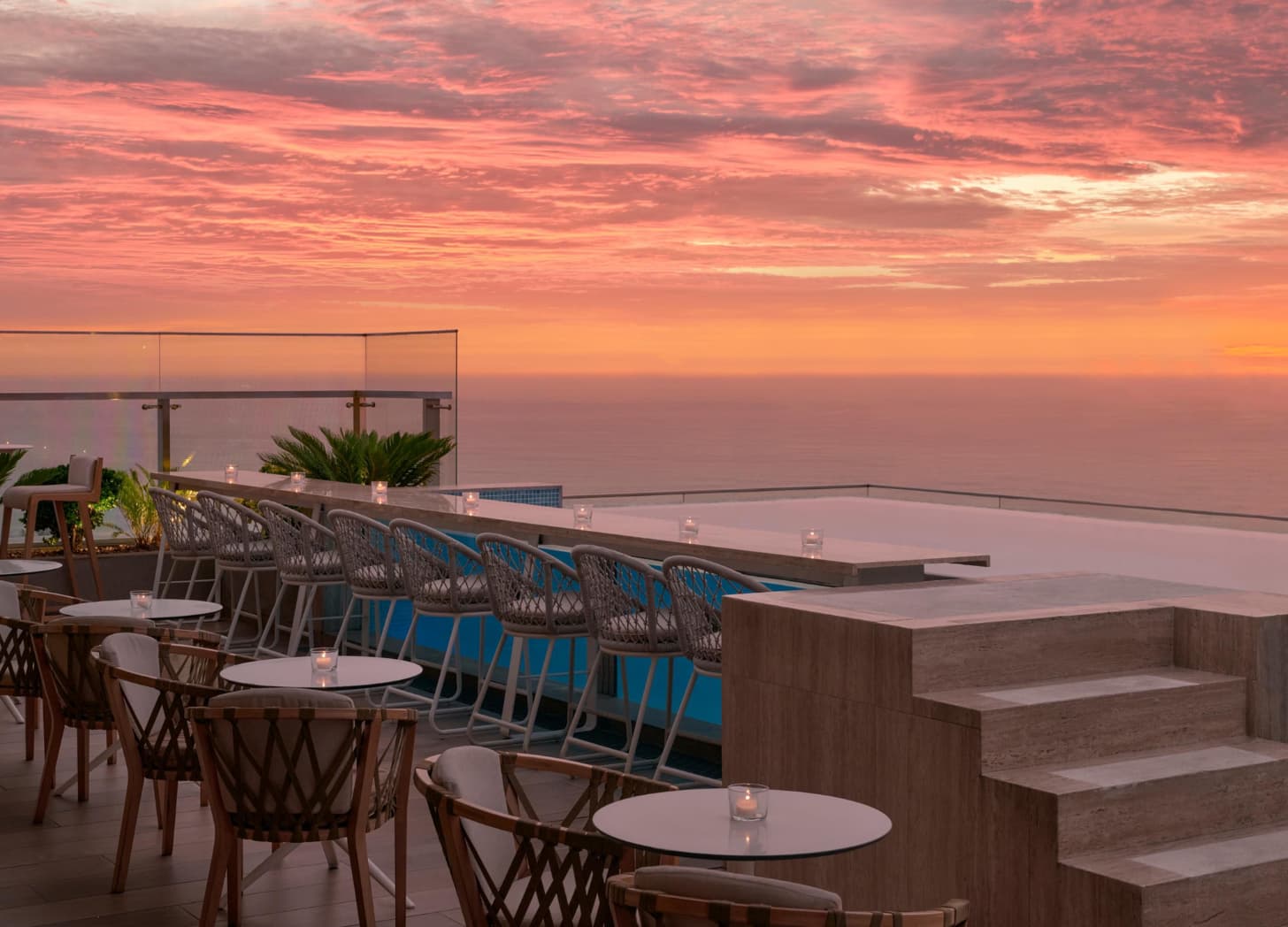 a rooftop patio with tables and chairs and a pool with a sunset