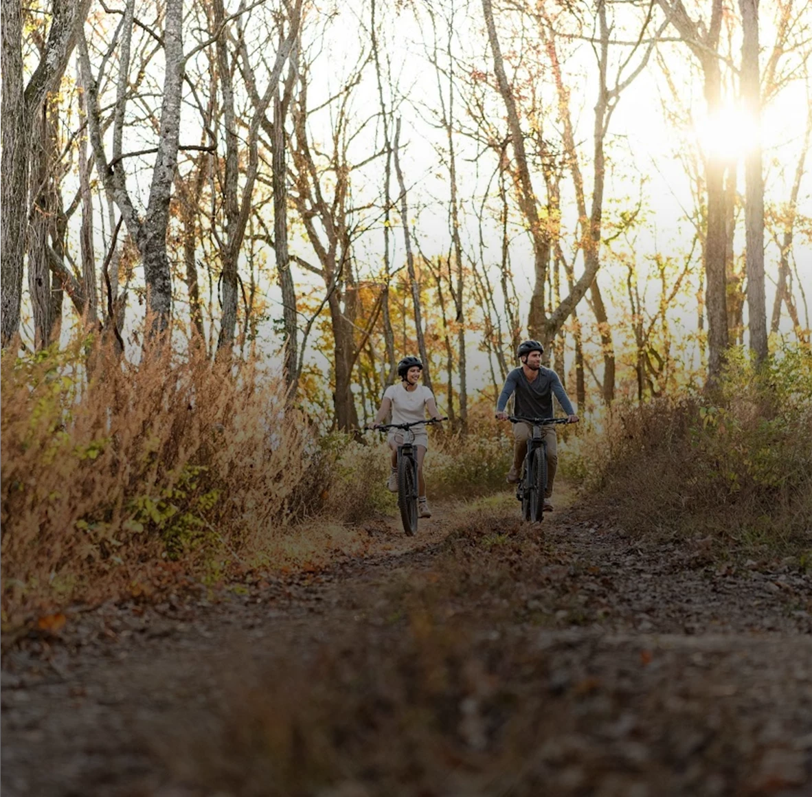a couple of people riding bikes on a dirt path through the woods