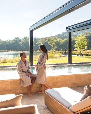 a man and woman in bathrobes sitting on a ledge by a pool