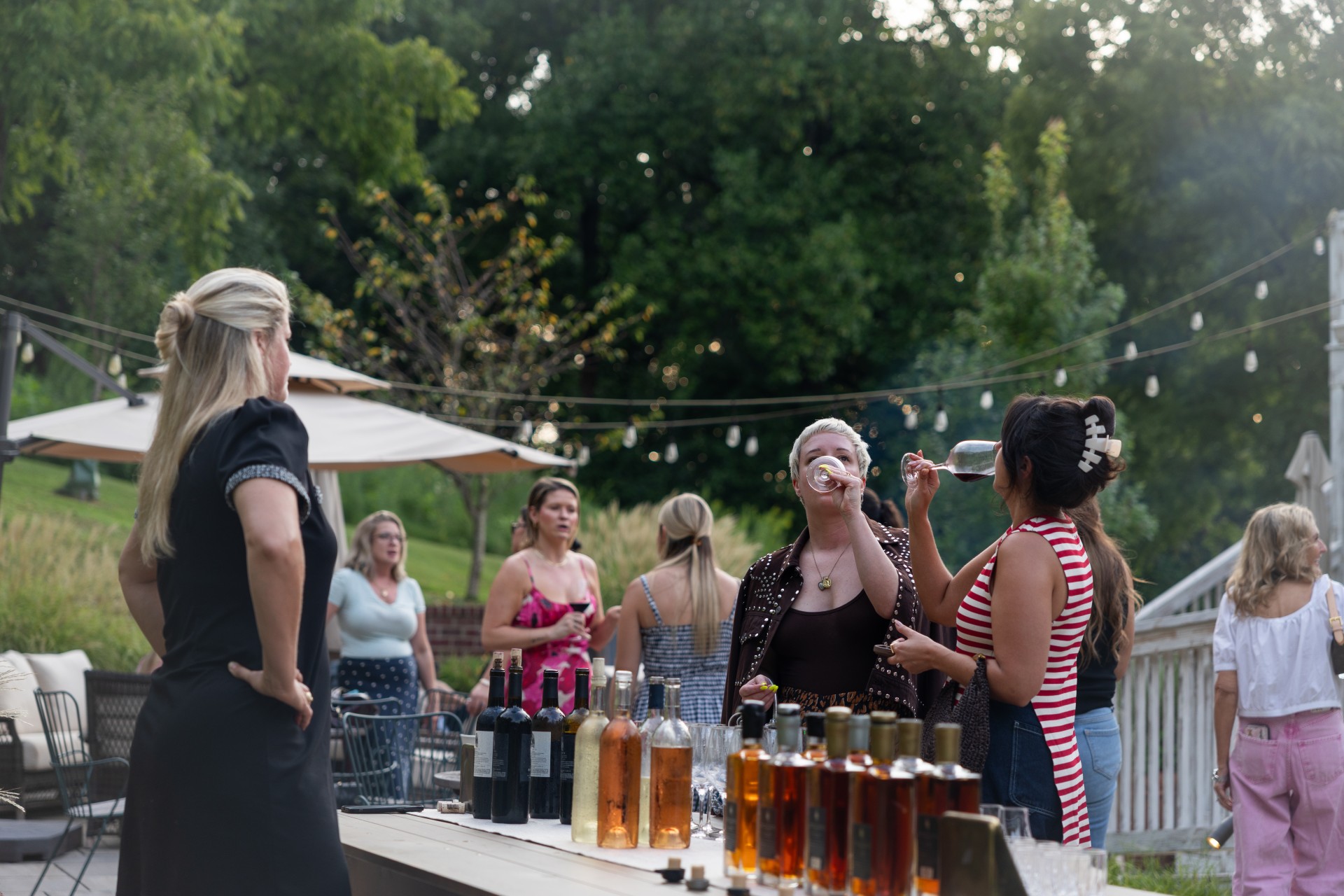a group of women standing around a table with bottles of wine
