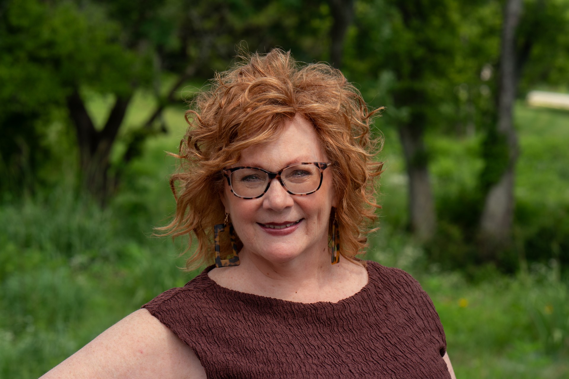 a woman with red hair wearing glasses and a brown shirt
