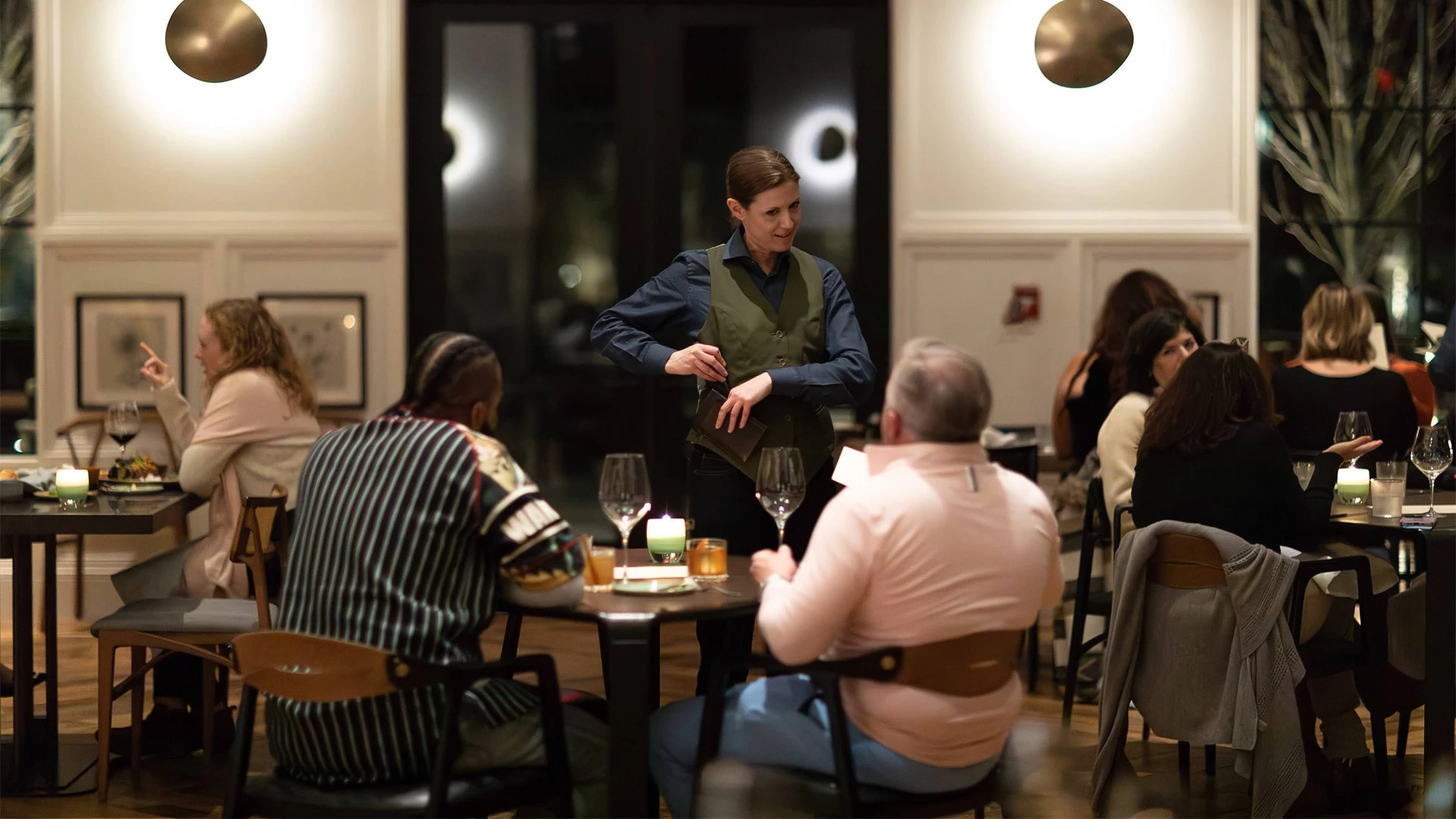 a woman standing at a table with people sitting around it