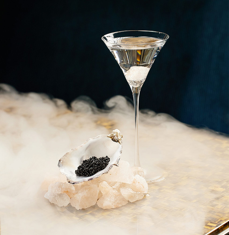 a glass of liquid with a shell on top of a rock