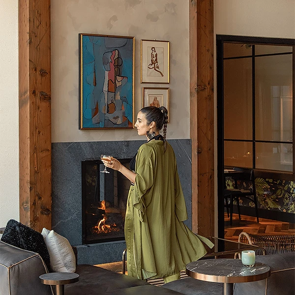 a woman holding a glass of wine in front of a fireplace