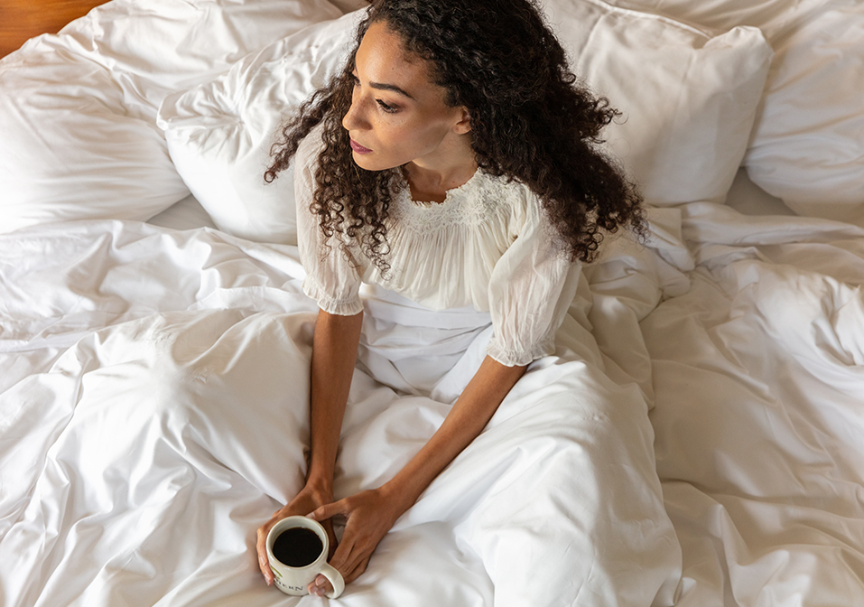 a woman sitting on a bed holding a cup of coffee