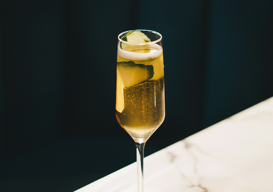a glass of champagne with a slice of cucumber