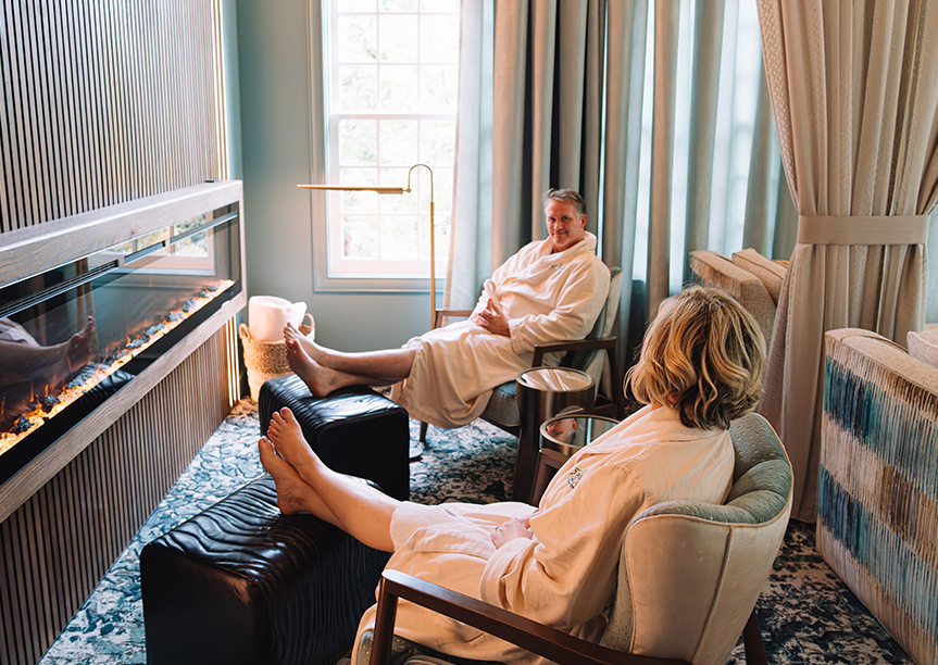 a man and woman in bathrobes sitting in chairs in a room with a fireplace
