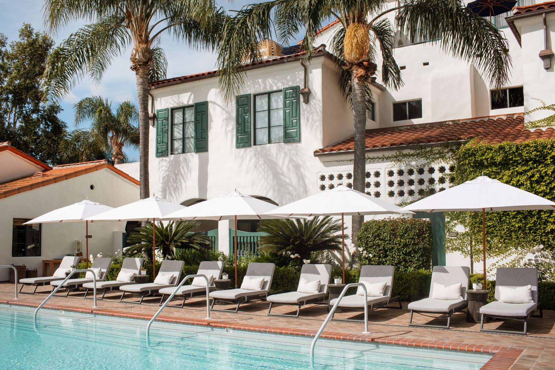 a pool with lounge chairs and umbrellas by a building