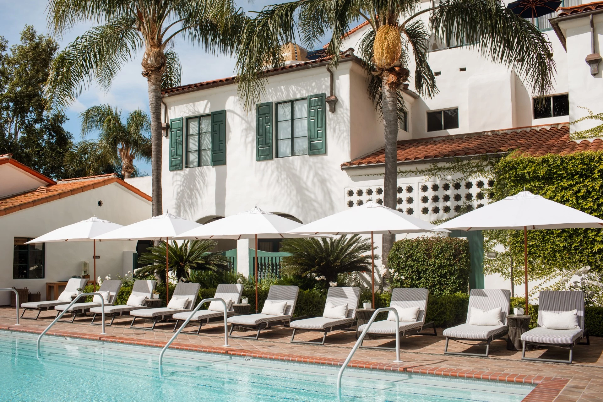 a pool with lounge chairs and umbrellas by a building