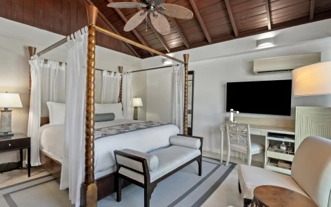 a room with a four poster bed and a desk and a fan