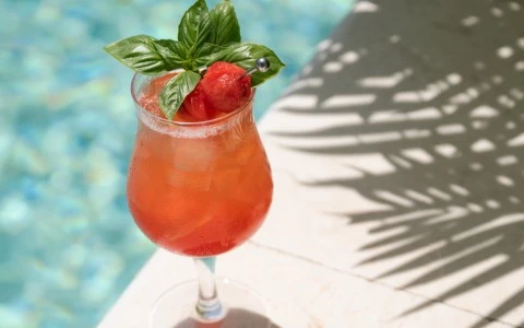 a glass of red drink with a cherry and basil leaf