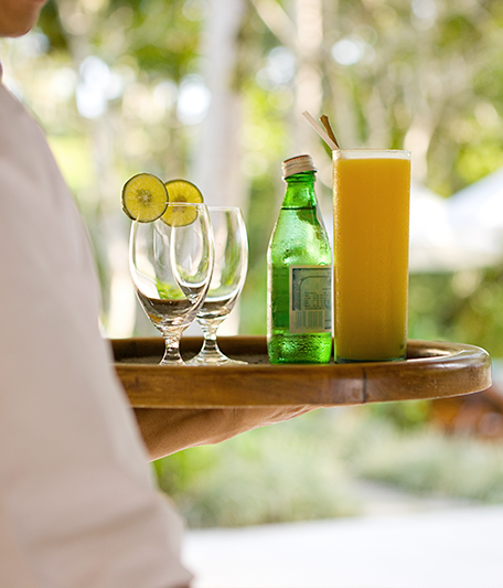 a person carrying a tray with a tropical beverage and two glasses