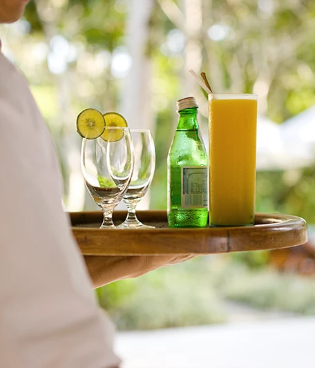 a person carrying a tray with a tropical beverage and two glasses