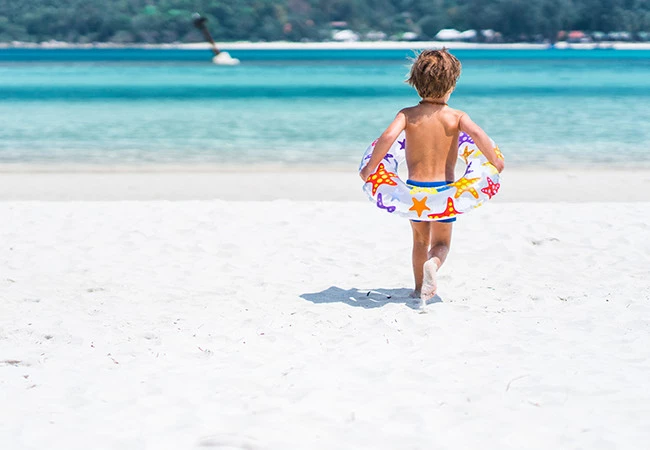 a little boy running to the water with a floating around his waist