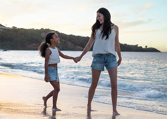 a woman and a girl holding hands on a beach