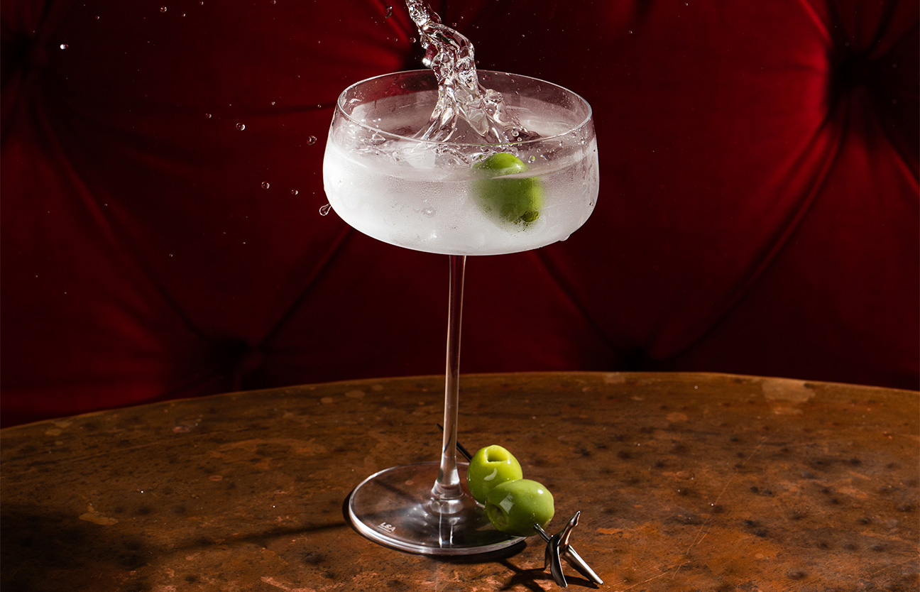 a glass with a drink and a green olive