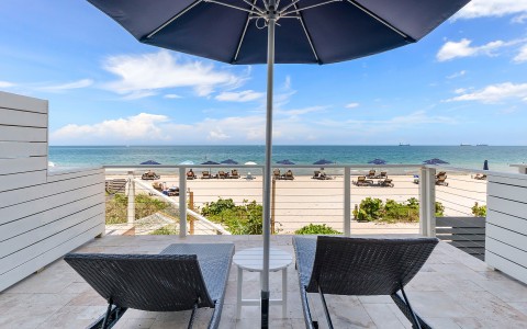 chairs and umbrella on a deck overlooking the ocean