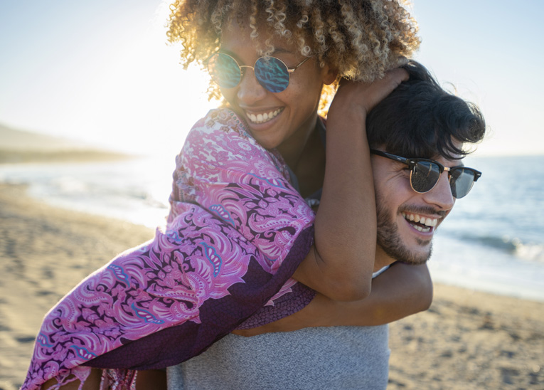 girl on the piggy-backing on a guy as he walks down the beach