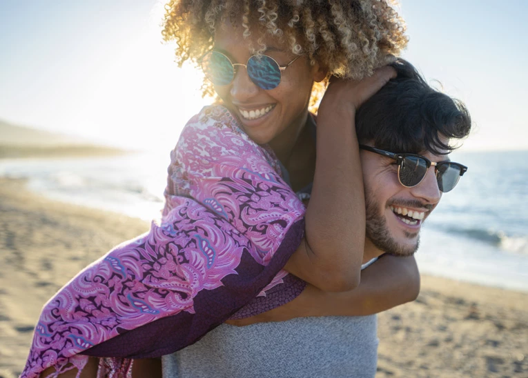 girl on the piggy-backing on a guy as he walks down the beach