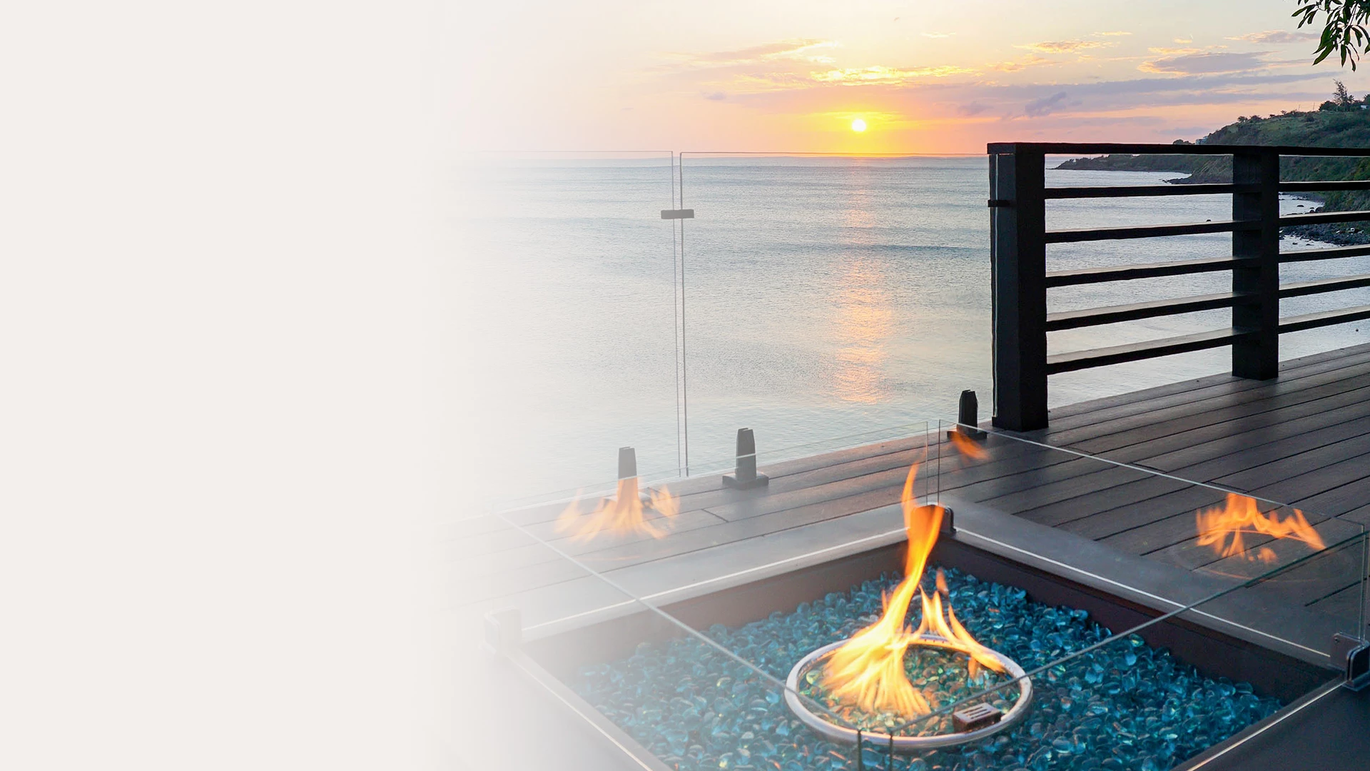 a fire pit on a deck overlooking the ocean and sunset