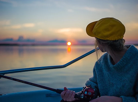 Woman holding fishing pole on boat with sun setting in the back