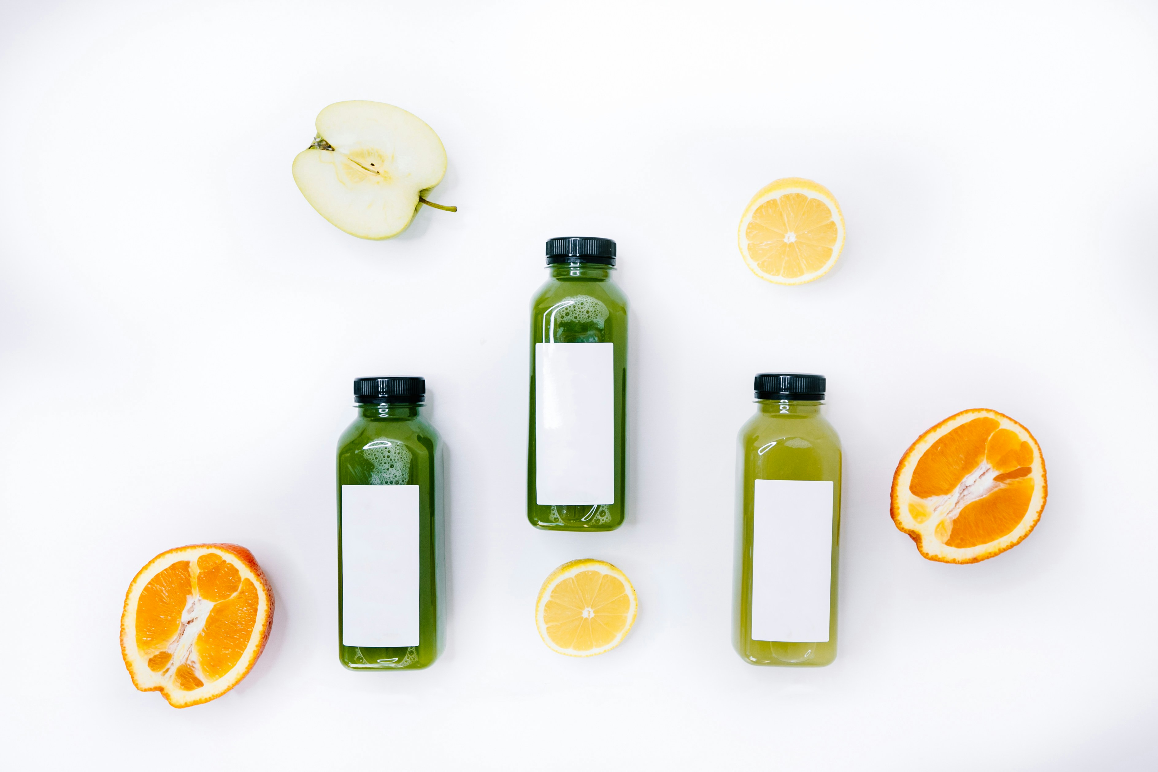 a group of bottles with green liquid next to sliced oranges and apples
