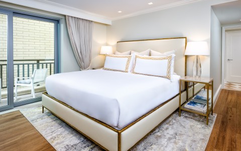 a bed with white sheets and pillows in a room with a glass door