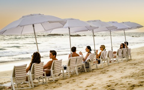 a group of people sitting in chairs on a beach with umbrellas