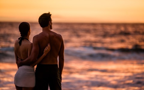a man and woman standing on a beach looking at the ocean