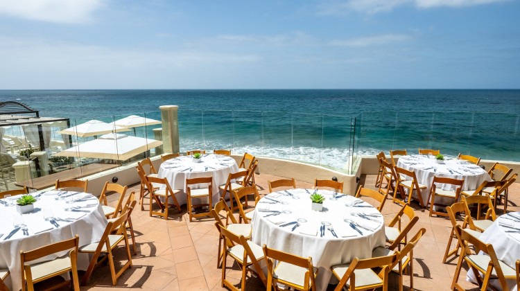 a table set up with white cloths and chairs on a patio overlooking the ocean