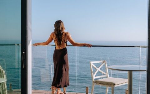 a woman in a dress standing on a balcony overlooking the ocean