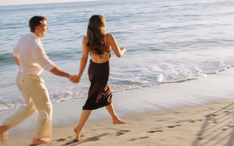 a man and woman holding hands on a beach