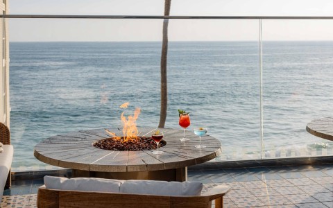 a fire pit with drinks on a patio overlooking the ocean