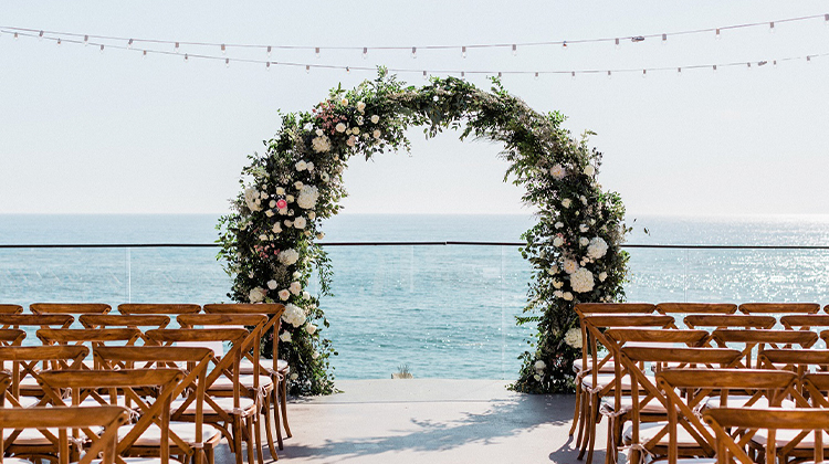 floral arbor surrounded by wooden chairs with a view of the ocean