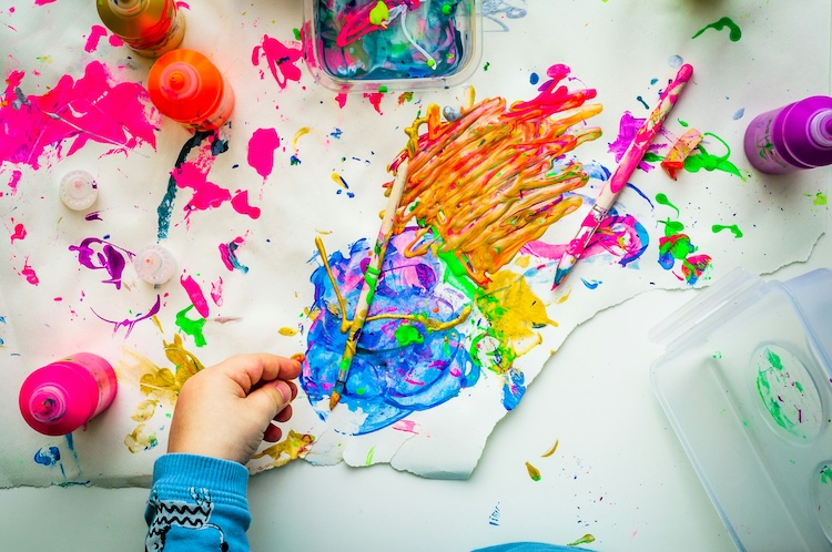 a child painting with paintbrushes and paint on a white surface