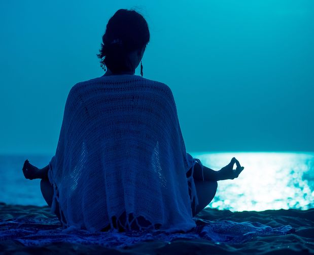 a person in a white coverup doing yoga during a full moon on a beach