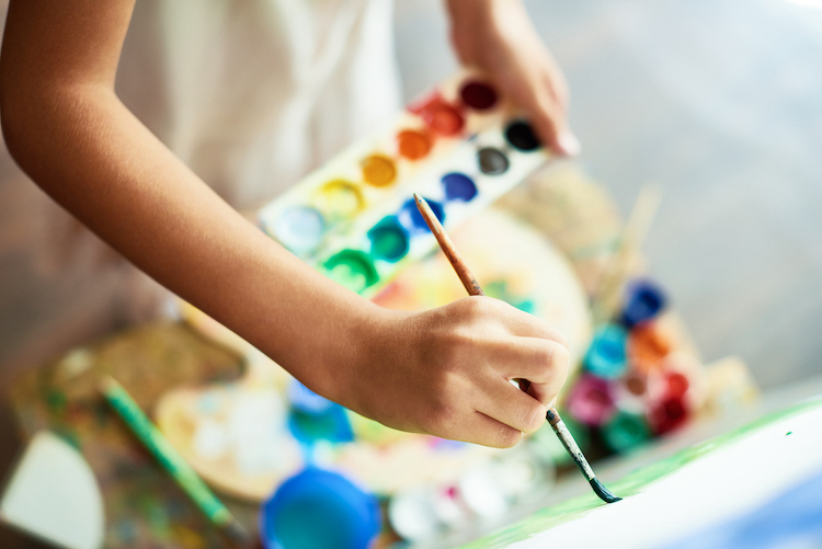 a hand holding a paintbrush and a palette of paint