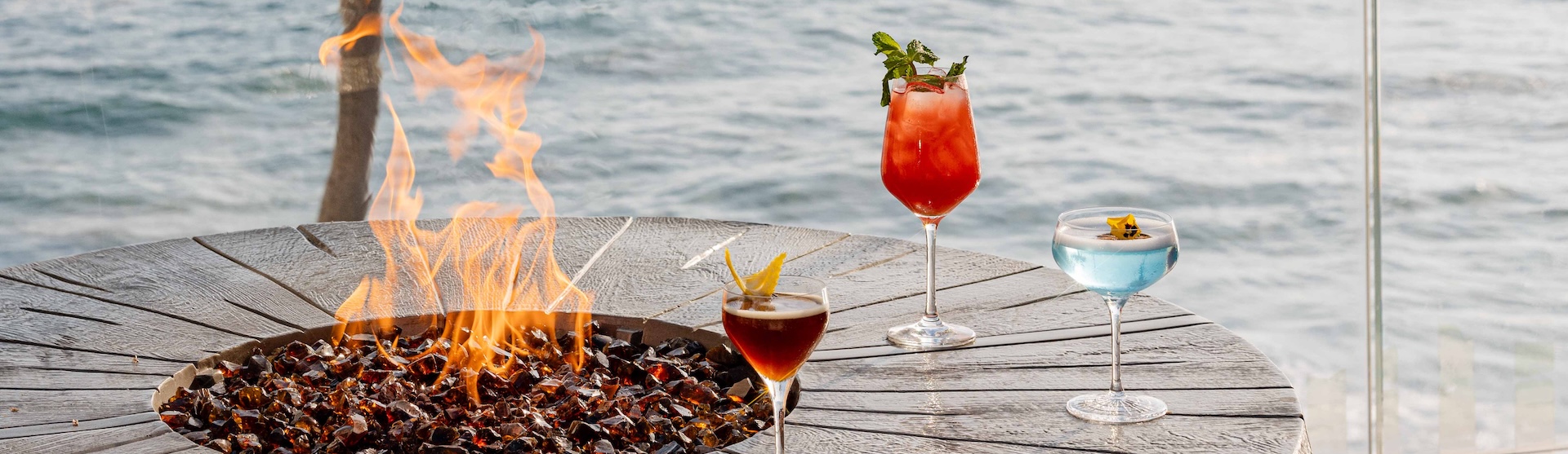 a two glasses of drinks on a table next to a fire pit