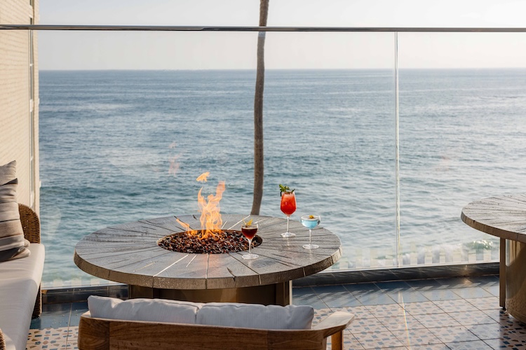 a fire pit with drinks on a patio overlooking the ocean