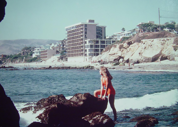 a person standing on a rock by the water with buildings in the background